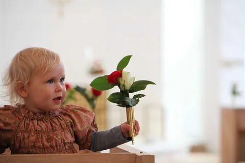 Kleines Kind im Hochstuhl mit zwei Blumen in der Hand